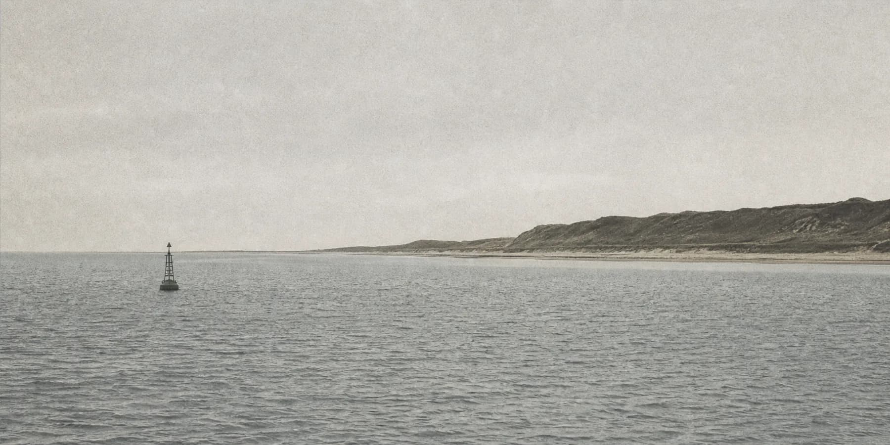 Coastal passage with low dunes and a channel marker buoy